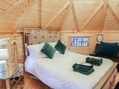 A bedroom with a bed with green pillows and folded towels a mirrored bedside table with a lamp and a window in a wooden room at Hexagon Hut - Dec Update in Dungiven Londonderry
