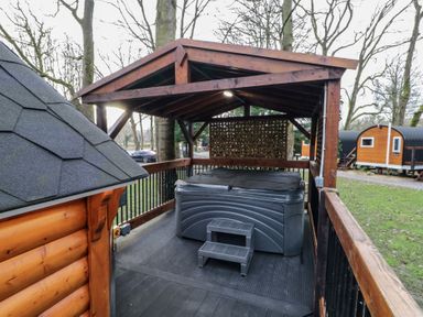 An outdoor covered hot tub on a wooden deck with trees and small cabins in the background at Hexagon Hut - Dec Update in Dungiven Londonderry