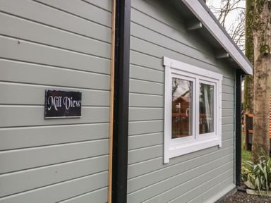 The exterior side wall of a building with a white-framed window and a sign that reads Mill View near two trees at Mill View in Dungiven Londonderry