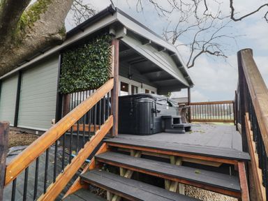 A raised wooden deck with stairs leading up to a covered area with a hot tub and outdoor seating surrounded by trees at Mill View in Dungiven Londonderry