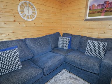 A blue sectional sofa with patterned cushions in a wooden paneled room with a clock and framed picture at Mill View in Dungiven Londonderry