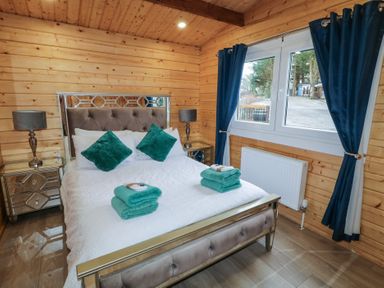 A bedroom with a double bed with teal pillows and towels two bedside tables with lamps and a window with blue curtains at Mill View in Dungiven Londonderry