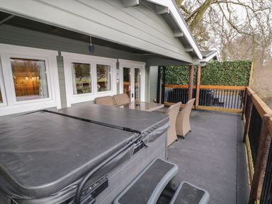 An outdoor covered deck with a hot tub and wicker chairs around a table at Mill View in Dungiven Londonderry