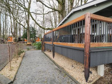 A gravel pathway next to a raised porch with wooden railing surrounded by trees and small wooden cabins at Mill View in Dungiven Londonderry