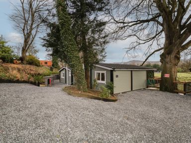 A gravel driveway with two small gray buildings surrounded by trees and a wooden fence at Owenbeg in Dungiven Londonderry
