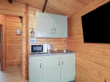 A kitchen area with a microwave kettle and sink mounted on cabinets and a wall mounted television at Owenbeg in Dungiven Londonderry