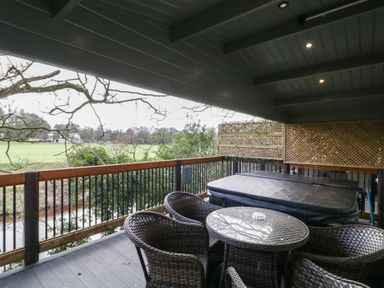 A covered balcony with a hot tub and wicker chairs around a glass table overlooking a field at Owenbeg in Dungiven Londonderry