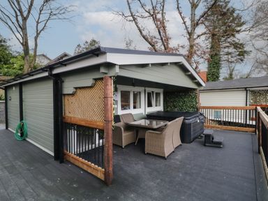 An outdoor deck with a green shed seating area table chairs and a hot tub at The Roe in Dungiven Londonderry