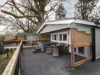 An outdoor deck area with a hot tub wicker chairs and a round table surrounded by trees at The Castle in Dungiven Londonderry