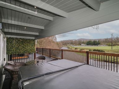 A covered balcony with a hot tub table and chairs overlooking a river and grassy field at The Castle in Dungiven Londonderry