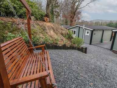A wooden swing bench on a gravel area with a green building in the background at The Castle in Dungiven Londonderry