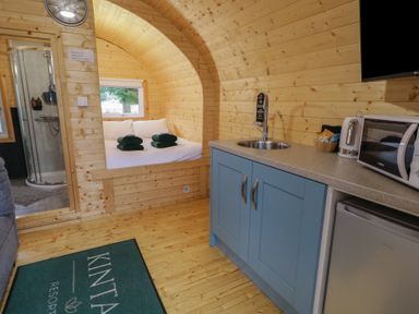 An interior view of a wooden cabin with a kitchen area a bed with towels and a bathroom with a shower at Hazel in Dungiven Londonderry