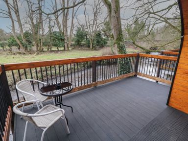 A balcony with two chairs and a round table overlooking a river and trees at Hazel in Dungiven Londonderry