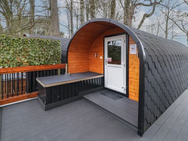 An outdoor wooden pod with a white door and black shingled roof surrounded by trees at Juniper in Dungiven Londonderry
