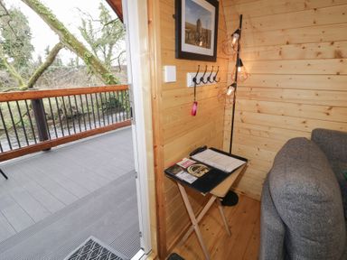 A wooden interior corner with a gray couch a small table with a binder and remote control a floor lamp and an open door leading to a deck over a river at Juniper in Dungiven Londonderry
