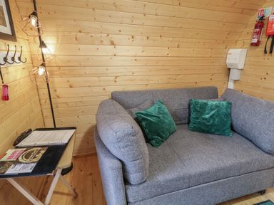 A corner of a room with a grey sofa with green cushions and a small table holding papers and a remote control at Juniper in Dungiven Londonderry