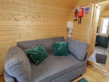 A wooden room with a gray sofa and green cushions next to a door leading to a bathroom at Juniper in Dungiven Londonderry