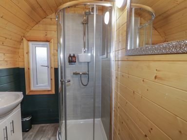 A bathroom with wooden panel walls a glass shower enclosure a white sink and a window at Juniper in Dungiven Londonderry