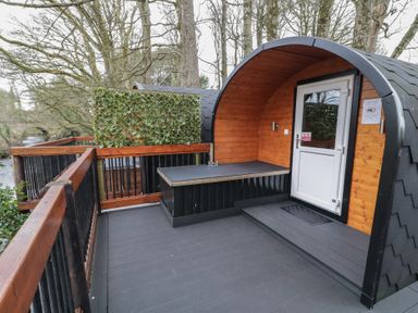 An outdoor wooden pod with a bench and white door on a deck surrounded by trees at Juniper in Dungiven Londonderry