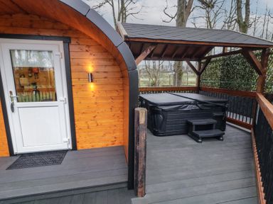 An outdoor wooden deck area with a covered hot tub and a small cabin with a white door at Birch in Dungiven Londonderry