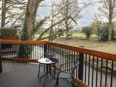 A balcony with a small round table and two chairs overlooking a creek and trees at Birch in Dungiven Londonderry