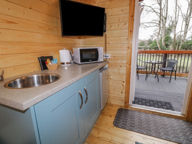 A small kitchenette with a sink microwave kettle and blue cabinets opening to a balcony with two chairs and a table at Birch in Dungiven Londonderry