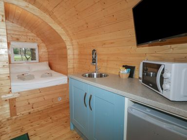 A wooden cabin interior with a bed towels kitchen sink microwave fridge and a wall-mounted TV at Birch in Dungiven Londonderry