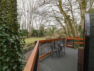 A wooden balcony with a small table and two chairs overlooking a river and trees at Birch in Dungiven Londonderry