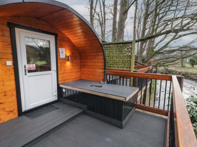A wooden pod with a white door on a deck with a countertop and railing by a river at Yew in Dungiven Londonderry