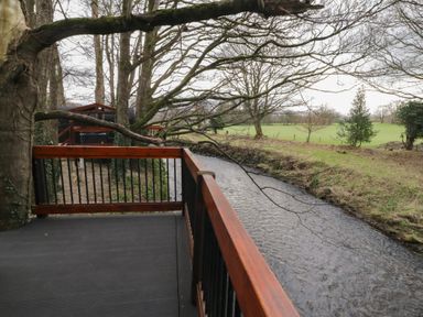 A wooden deck overlooking a river with trees and grass in the background at Yew in Dungiven Londonderry