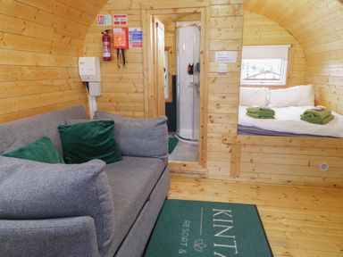 A wooden cabin interior with a gray sofa with green pillows a bed with folded towels and a shower enclosure at Yew in Dungiven Londonderry