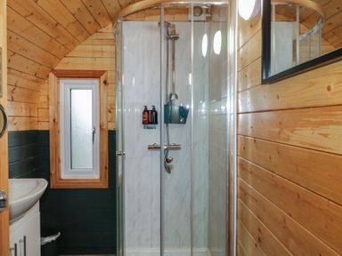 A bathroom with a wooden arched ceiling a glass shower enclosure a small window and a white sink at Yew in Dungiven Londonderry