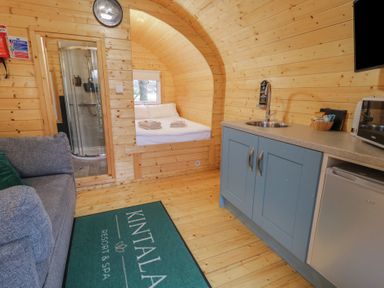 A small wooden room with a kitchenette a gray sofa a bed with white linens and a shower visible at Kintala Resort and Spa