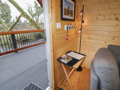 A small wooden corner with a foldable table holding papers and a remote beside a gray sofa and a door opening to a balcony with a river view at Hawthorn in Dungiven Londonderry
