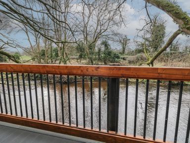 A wooden balcony railing with vertical black metal bars overlooking a river and trees at Hawthorn in Dungiven Londonderry