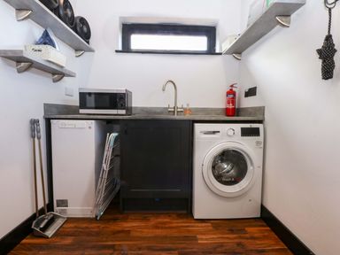 A laundry room with a washing machine and microwave at Y Cwt, Moelfre