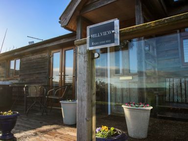 A wooden porch with glass doors, outdoor chairs, tables, and flower pots at Hillview in Stottesdon near Cleobury Mortimer