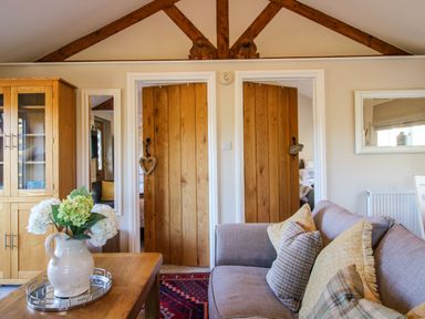 A sitting room with a sofa pillows wooden doors a cabinet and flowers on a table at Hillview in Stottesdon near Cleobury Mortimer