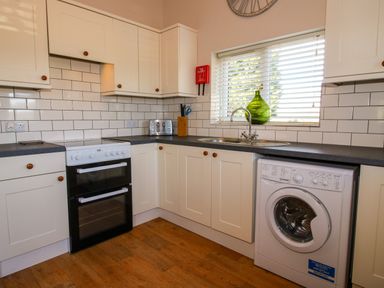 A kitchen with white cabinets a black countertop a stove a toaster a sink with a window above and a washing machine at Hillview in Stottesdon near Cleobury Mortimer
