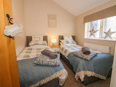 A bedroom with two single beds side by side with pillows and blankets a bedside table with a lamp and two decorative stars on the window at Hillview in Stottesdon near Cleobury Mortimer