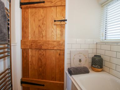 A bathroom with a wooden door a towel rail and a bathtub with a gray towel and decorative items at Hillview in Stottesdon near Cleobury Mortimer