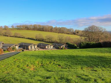 A field with green grass and a group of small buildings with hills and trees in the background at Hillview in Stottesdon near Cleobury Mortimer