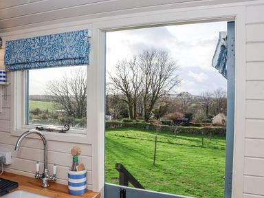 A kitchen sink area with a window and open door showing a green lawn and trees outside at Teg Prospidnick near Porthleven