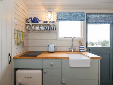 A kitchen with a wooden countertop a white sink blue cabinets and blue and white striped cups and a door at Teg in Prospidnick near Porthleven