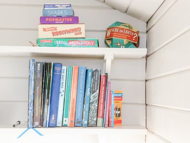 A bookshelf with board games and books on two white shelves at Teg in Prospidnick near Porthleven