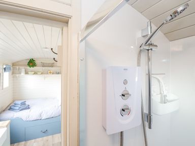 A bathroom with a shower unit next to a bedroom with a bed and shelves at Teg in Prospidnick near Porthleven