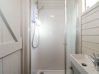A shower with a glass door next to a small sink in a bathroom at Teg in Prospidnick near Porthleven