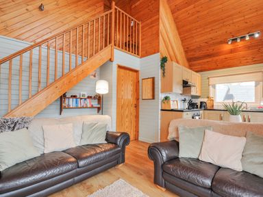 A living room with a staircase and kitchen at Cornish Woodland Retreat Near St Tudy