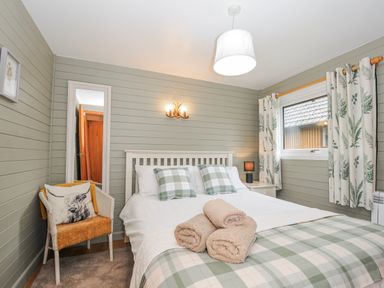 A bedroom with a bed, bedside table, and curtains at Cornish Woodland Retreat Near St Tudy