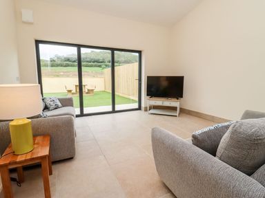 A living room with grey sofas a television on a stand and a lamp on a wooden side table at Bears Court Barn 3 Little Rissington near Bourton-On-The-Water